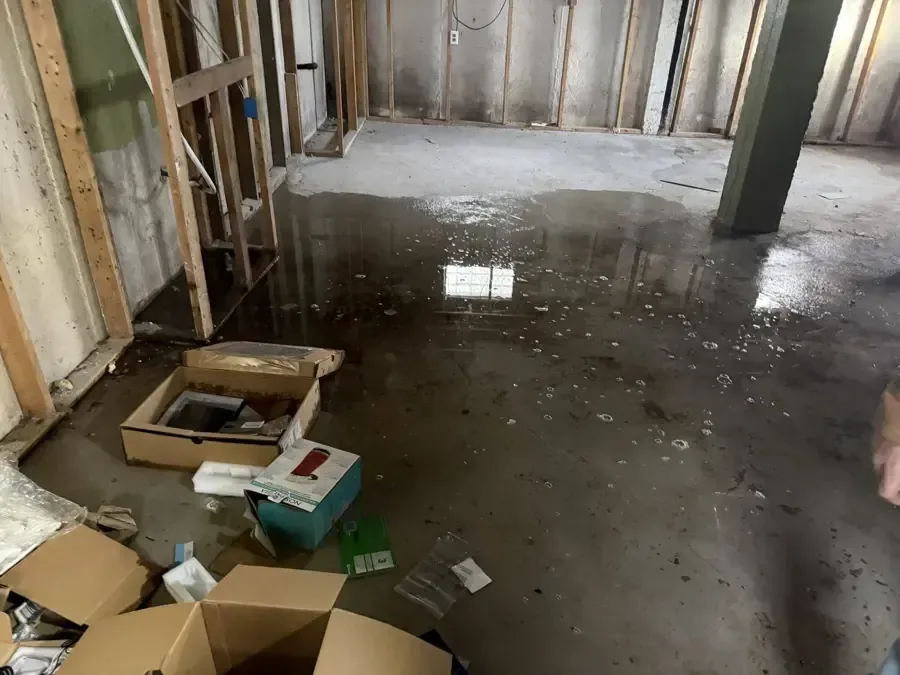 Standing water across an unfinished basement floor with wet boxes